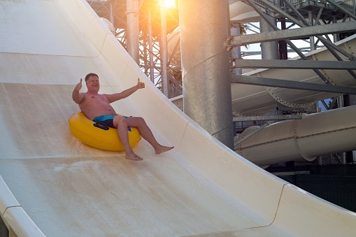 An adult man happily rides on a ring on a water slide in a water park.