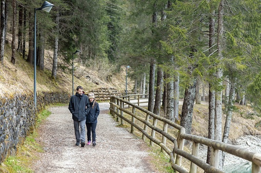 Young couple walking embraced on pathway by Auronzo Lake, in Auronzo di Cadore village; Belluno, Dolomites, Italy