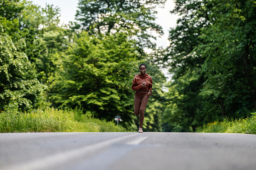 Shot of a smiling young woman enjoying running on a scenic route. Cropped shot of a young woman running at full pace on a scenic route in the nature in the background.