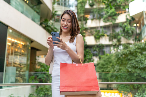 Young Asian Woman in Casual Outfit, Juggling Shopping Bags and Smartphone - Enjoying a Casual Shopping Spree in the Mall