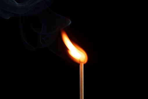 A yellow and orange  flame coming from an ignited wood match. Blue background ... Copy space on the flame.