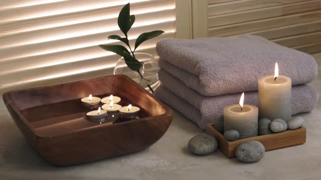 Beauty spa treatment items on white wooden table. Candles, stones, bowl with water and towels. Cozy bath.