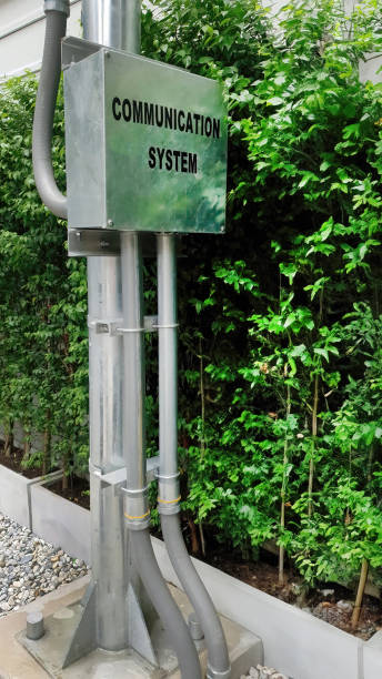 istock Outdoor control metal box of communication system hub and vertical ducts for cables installed on pole with green tree background, construction business 1804128887