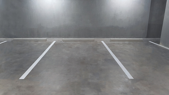 Underground vacant parking lot in building basement, white color painted marking line on exposed concrete polished cement floor, construction finishing material