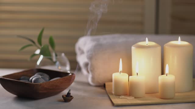 Beauty spa treatment items on white wooden table. Candles, stones, incense cone and towel. Cozy bath.