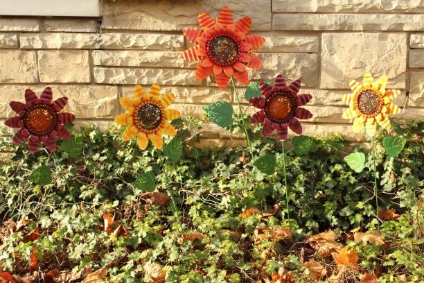 Five metal sunflowers stand in a garden in front of a tan stone wall