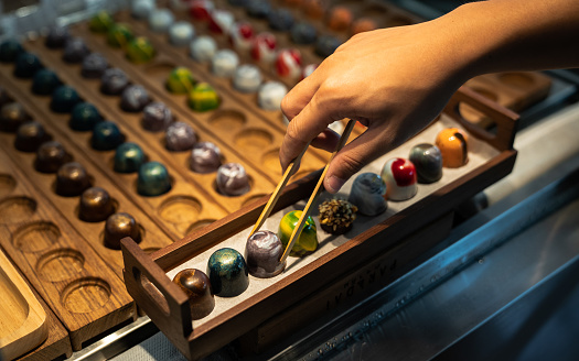 Baker or chocolatier taking handcrafted chocolate bonbons from shelf store.