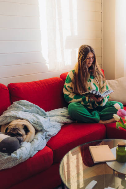 istock Woman Relaxing on Red Sofa with Her Dog Enjoying Reading 1804166436