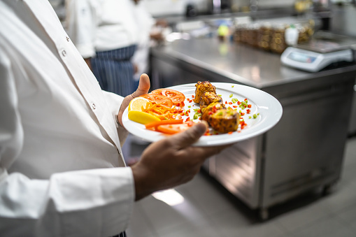 An appetizer of freshly cooked tandoori chicken with tomato and lemon on a white plate being carried by a pair of hands