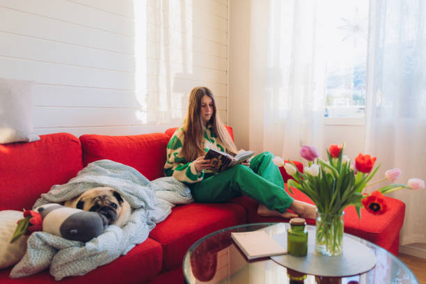 istock Woman Relaxing on Red Sofa with Her Dog Enjoying Reading 1804169224