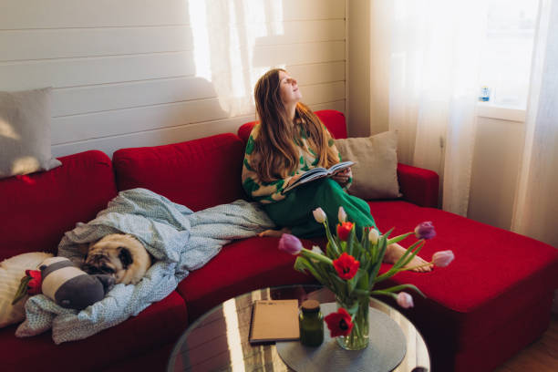 istock Woman Relaxing on Red Sofa with Her Dog Enjoying Reading 1804169754