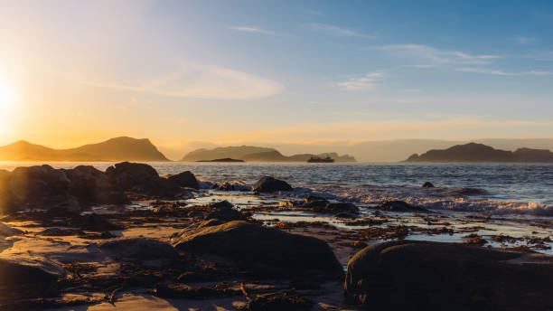Dramatic view of a boat sailing on the wavy sea with view of the islands and the mountains during dramatic winter sunset in the Western fjords of Norway