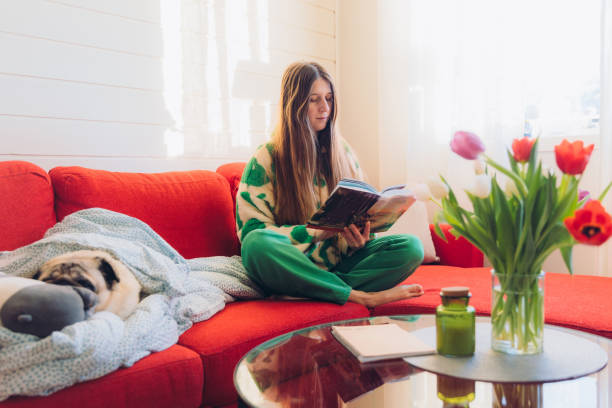 istock Woman Relaxing on Red Sofa with Her Dog Enjoying Reading 1804170828