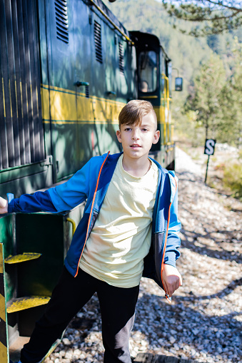 Cute schoolboy riding a historic narrow track train. Boy is ready for an adventure of a lifetime. Train station on a sunny autumn day.