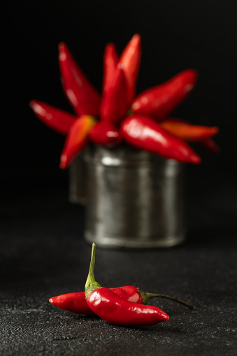Spicy red chillies in an old metal measuring container on a black background.