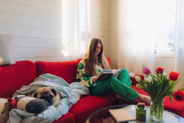 istock Woman Relaxing on Red Sofa with Her Dog Enjoying Reading 1804176742