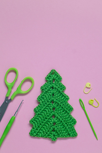 Handmade green crochet Christmas tree and crochet tools on a lilac background. Top view. Copy space.