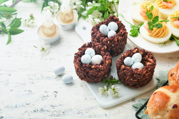istock Easter brunch or breakfast. Easter chocolate nest cake with chocolate candy eggs, traditional hot cross buns and deviled eggs with bouquets of blooming apple trees. Spring Easter holiday food concept. 1804206697