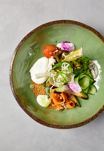 Salad bowl with salmon, avocado, broccoli, vegetables and egg on homemade ceramic plate. Buddha bowl with salmon, broccoli, quinoa in modern serveware. Modern ceramic dishware on concrete background