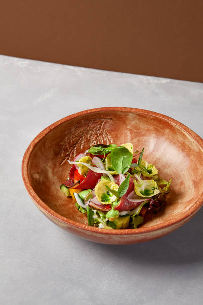 istock Salad with pastrami, vegetables and dressing on handmade ceramic bowl. Vegetables salad with roast beef in modern dishware on gray stone background. Contemporary food from chef. Handmade dinner plate. 1804239638