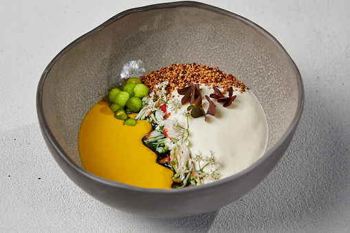 Pumpkin soup with crab in handmade ceramic bowl. Innovative recipes - cream soup with crab and cheese espuma on white concrete background. Modern food in dishware