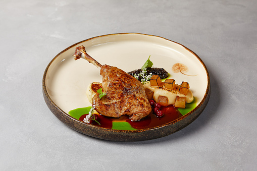 Duck confit with celery mash, cranberry and pear in handmade ceramic plate. Duck leg on modern dishware with hard shadow