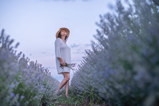 Lady in White in Levander Field. She is wearing a white dress and a straw hat and is holding a bouquet of lavender in her hands.