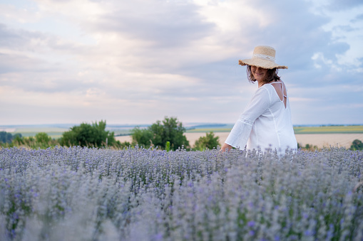 A young woman in a lavender field against a romantic sky. She is wearing a white dress and a straw hat.