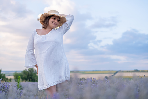 A young woman in a lavender field against a romantic sky. She wears a straw hat.