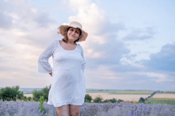 A young woman in a lavender field against a romantic sky. She wears a straw hat.