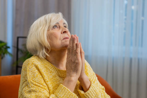 istock Worried senior elderly woman praying sincerely with folded arms asking God for help, begging apology 1804274121