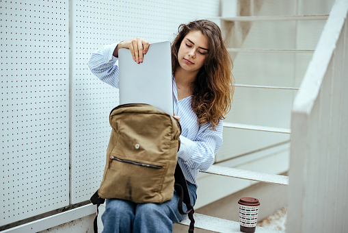 Young woman sits on the stairs and takes out a laptop from her backpack
