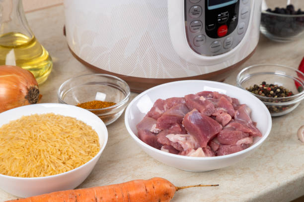 istock Prepared ingredients for cooking pilaf in modern multi cooker in kitchen on a table. Cooking pilau with meat in multicooker. 1804289037
