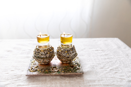 A pair of Shabbat candles are lit with oil on silver candlesticks on the Shabbat table