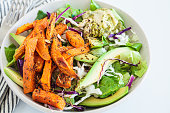 Baked sweet potato wedges with avocado and hummus. Healthy vegan lunch salad.