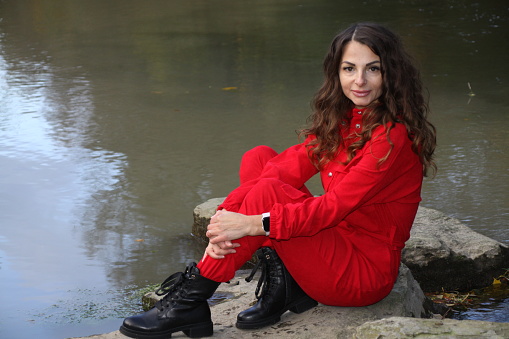 Portrait of an attractive, pretty woman in red overalls, posing on a stone in the river, close to paderborn