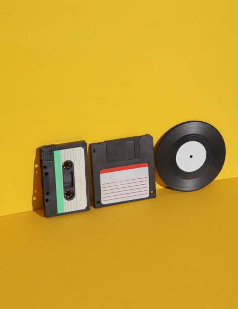 istock Outdated technologies. Retro 80s audio cassette with floppy disk and vinyl record on yellow background with shadow. Creative layout 1804339603