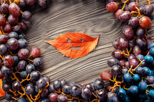 Bright autumn background of grapes with a copy of the space. Top view. bright autumn leaf with a symbolic smile on a dark wooden background.