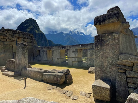 A tranquil and serene scene of the historical Temple of Three Windows in Machu Picchu, with a dramatic backdrop of mountains and clouds