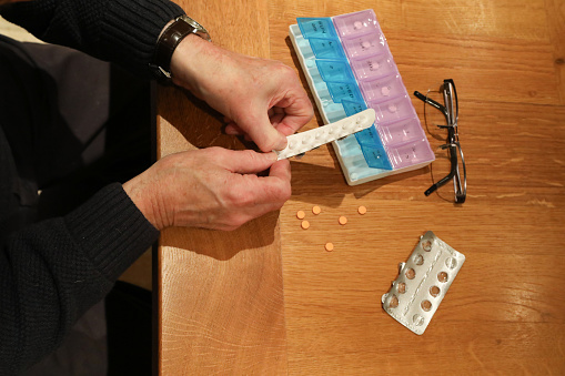 Senior male pensioner preparing daily medication for age-related health conditions in pill box organiser