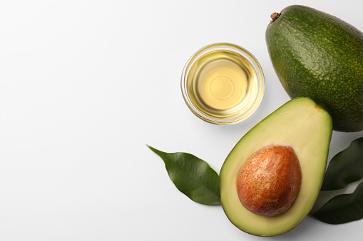 Cooking oil in bowl and fresh avocados on white background, flat lay. Space for text