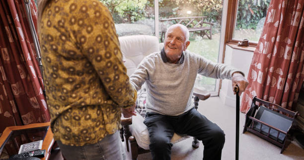老人は、杖とサポートで退職した介護者と家で話したりリラックスしたりします。先輩、人、女性との会話 アパート、居間、家で気遣いと話し合い - old armchair women senior adult ストックフォトと画像