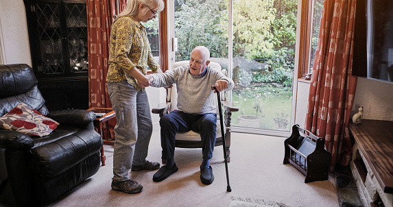 Elderly, couple and help with walking stick for care, support or assistance on sofa in living room of home. Senior, woman or man with disability or cane in lounge of retirement with love and recovery