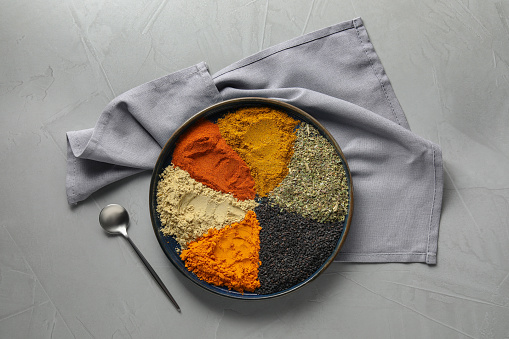 Plate with different spices on light grey table, flat lay