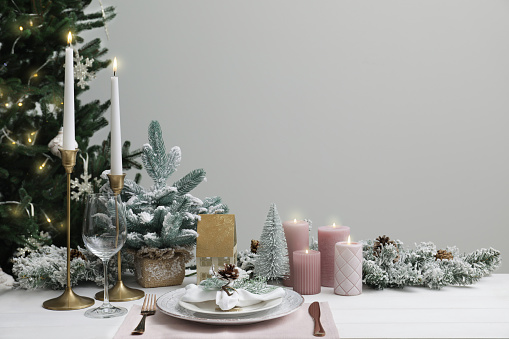 Festive place setting with beautiful dishware, cutlery and cone for Christmas dinner on white wooden table. Space for text