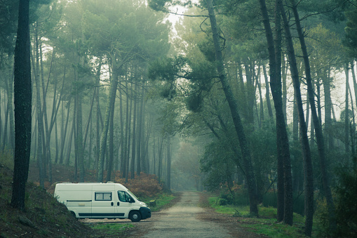 Photograph of a white camper van. Mobile home in pine forest at dawn with fog. Traveler nomadic lifestyle