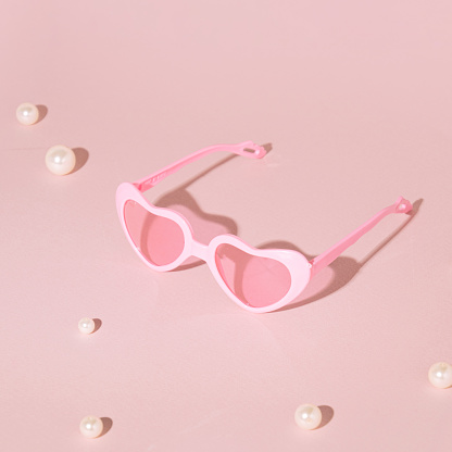 Heart shaped sunglasses and pearl beads, creative summer holidays composition,minimalistic style, pale pink background.
