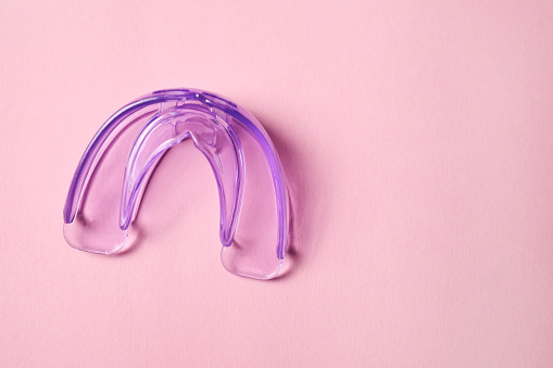 Transparent dental mouth guard on light pink background, top view with space for text. Bite correction