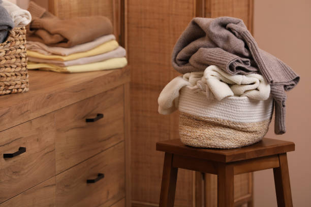 istock Wicker laundry basket overfilled with clothes on wooden stool indoors 1804451416