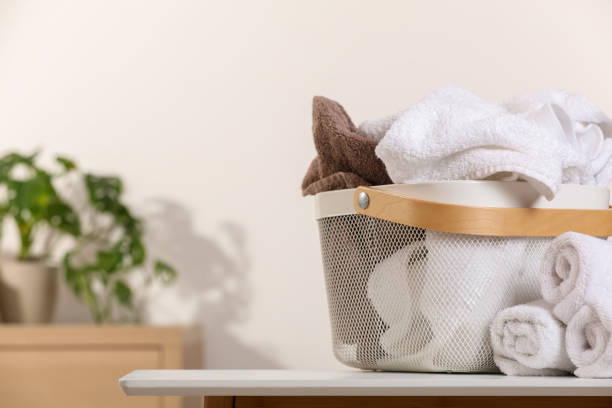 istock Laundry basket overfilled with clothes near rolled towels on white table indoors. Space for text 1804451949